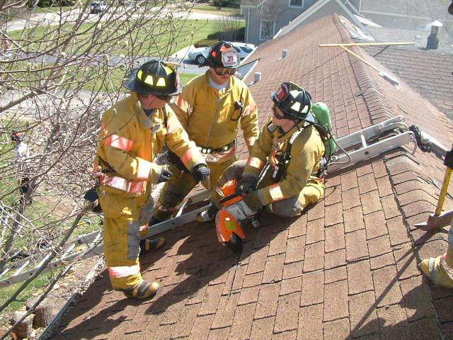 Firefighter practicing ventilation of roof on home scheduled for demolition